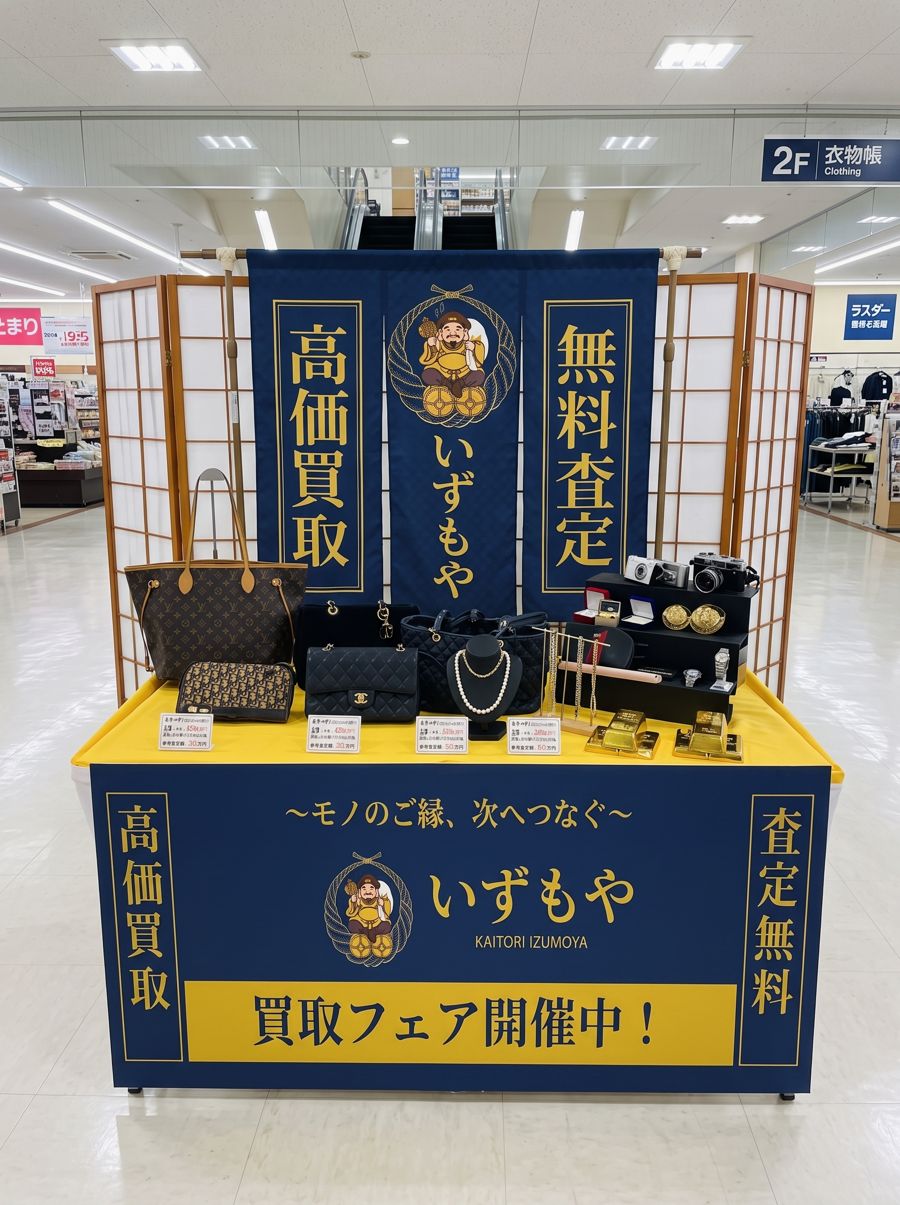商業施設の催事場に設けたいずもやの買取ブース。紺地に金文字ののれんと巻き幕、黄色のクロスを掛けた陳列机